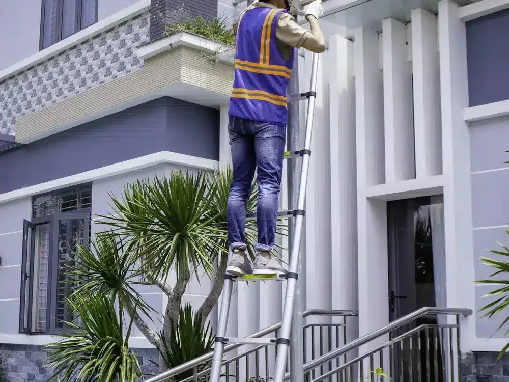 Technician on a ladder treating a nest high on a two storey home